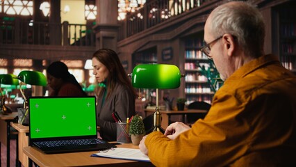 Senior male learner studying academic materials with green screen on laptop, collecting important information for exams and thesis completion. Old man serious about graduating college.