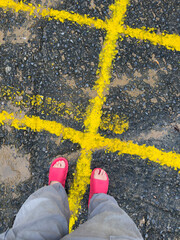 top view of men's legs dressed in gray trousers and pink sandals, yellow road markings on the asphalt