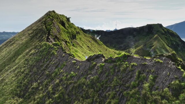 Man running rugged, green covered hills ridge crater rim of Mount Batur volcano, caldera and steaming vents in Bali, Indonesia. Active sports, travel, hiking outdoor. Aerial drone flight panorama