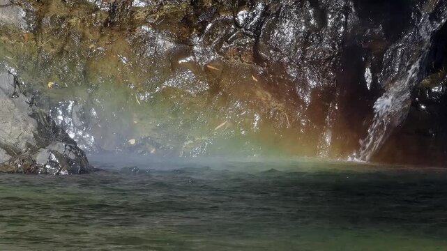 Waterfall is bathed in sunlight, creating a rainbow in the afternoon.