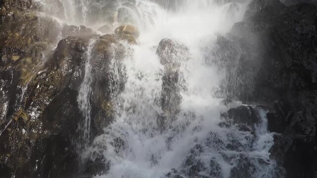 Waterfall is bathed in sunlight, creating a rainbow in the afternoon.