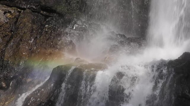 Waterfall is bathed in sunlight, creating a rainbow in the afternoon.