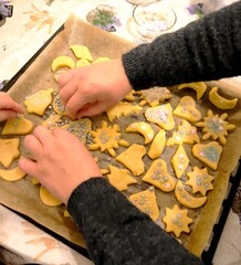 Children's hands decorate raw cookies with stars and sprinkles.