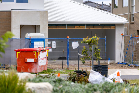 Residential construction site in a modern Australian suburb, with a skip bin, safety fencing, and building materials placed in front of a partially completed house. Renovation waste management