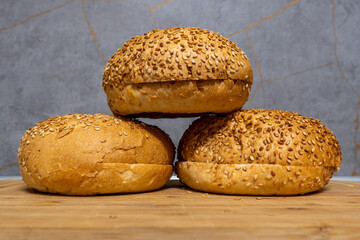 Three round bread rolls with sesame seeds on wooden surface against textured background in indoor setting