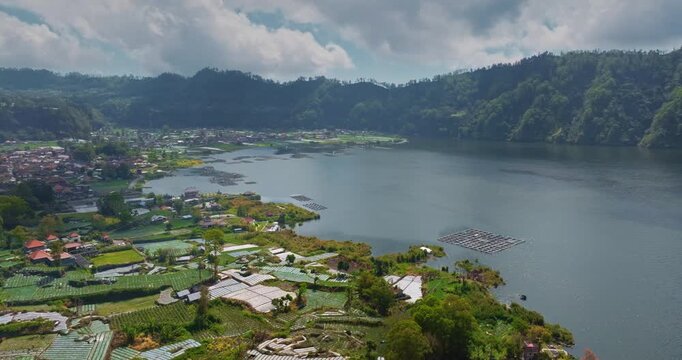 Indonesia, Bali, Abang: Panoramic aerial view Lake Batur with its floating fish farms, surrounding villages and extensive agricultural terraces on the fertile volcanic slopes. Aerial drone flight