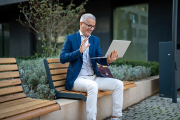 Fototapeta premium Mature businessman waving during outdoor video call