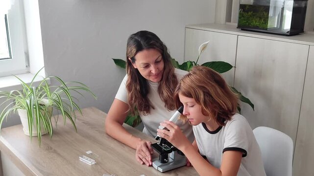 Cute girl with smiling mother enthusiastically studying plants under child microscope. Family having fun discovering world of plants through the lens of optical magnifying instrument