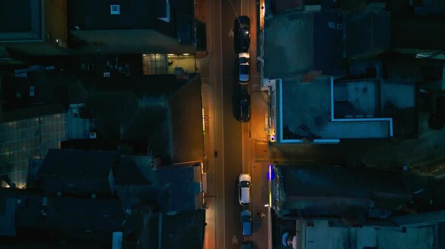 Aerial view of a street at night, with cars and buildings illuminated by streetlights.