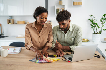 Black couple designing home interior using color palette and laptop