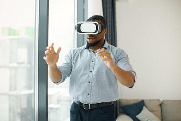 Black male entrepreneur standing near big windows wearing virtual reality glasses