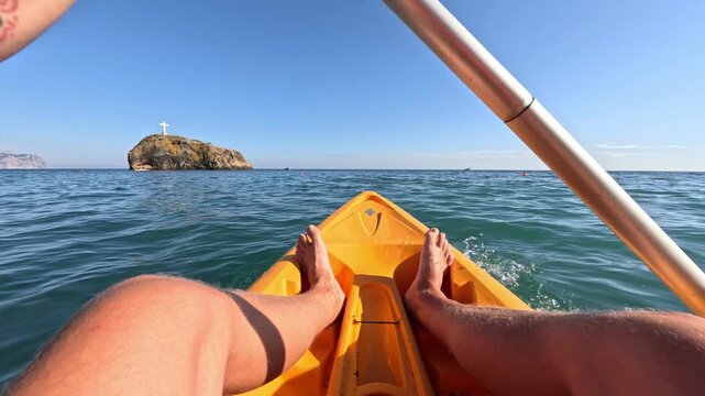 Kayaking paddling sea, point of view of a person rowing a yellow kayak towards a scenic island on a sunny day.