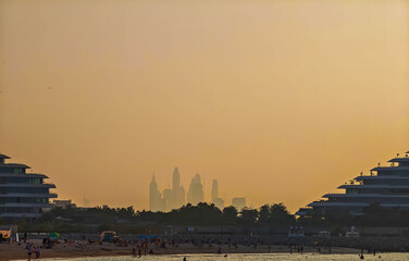 Dubai Marina skyline at sunset viewed from Jumeirah Beach with glowing city silhouettes. Golden hour view