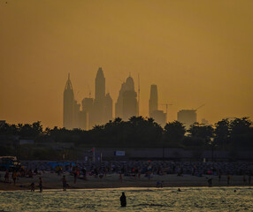Dubai Marina skyline at sunset viewed from Jumeirah Beach with glowing city silhouettes. Golden hour view