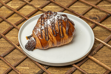 A croissant filled with hazelnut cream and sliced ​​banana, accompanied by chocolate syrup and...