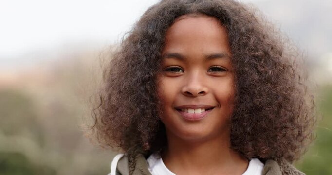 School-age boy standing on hillside noticing camera and shifting expression into broadening smile