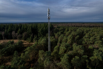 Aerial landscape with radio tower technical antenna communication and data transmission in Veluwe nature Dutch moorland park forest side lit contrasting green against blue sky