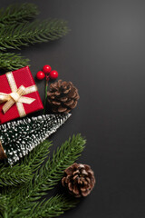 Christmas flat lay with red gift box, pinecones, fir branches, berries, and mini trees on black background. Perfect for elegant holiday greeting cards, festive promotions, and seasonal design.