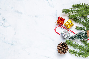 Flat lay of Christmas decorations with fir branches, pine cone, gift boxes, and candy canes on white marble background. Perfect for holiday greeting templates, winter design, and festive ads.