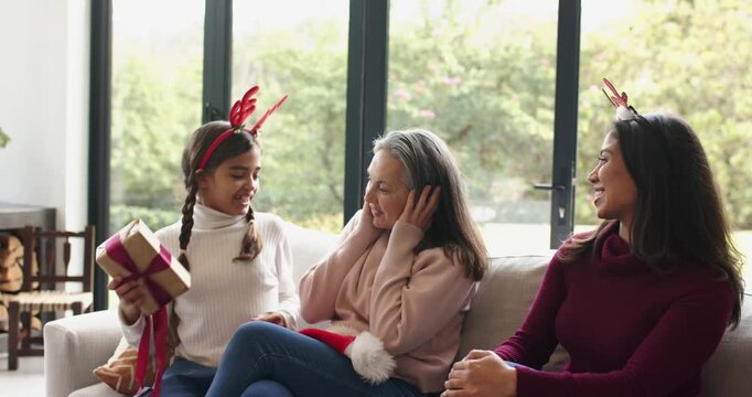 Three-generation family celebrating arrival and smiling while grandchild handing gift on sofa