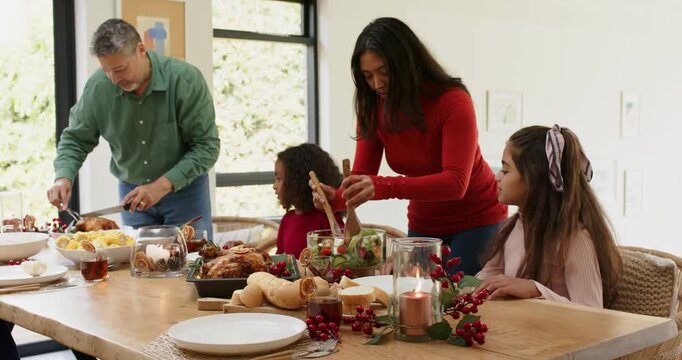 Diverse family gathering at table father carving turkey and mother tossing salad for holiday meal