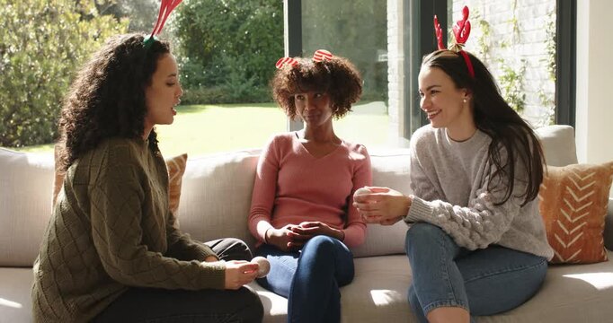 Diverse female friends breaking silence on sofa sharing animated anecdote with headbands and mug