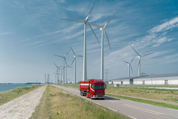 A red truck in front of the port in Borssele. In the background, wind turbines, the port, and a cargo ship.