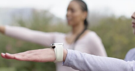 Vibrating smartwatch alert guiding Diverse female friends stretching arms for yoga practice in park
