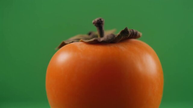 Vibrant, ripe orange persimmon fruit close-up, highlighting natural texture and rich color, isolated on bright green, perfect for healthy food and fresh eating concepts