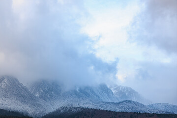 Majestic snow-capped mountains shrouded in misty clouds under a blue sky