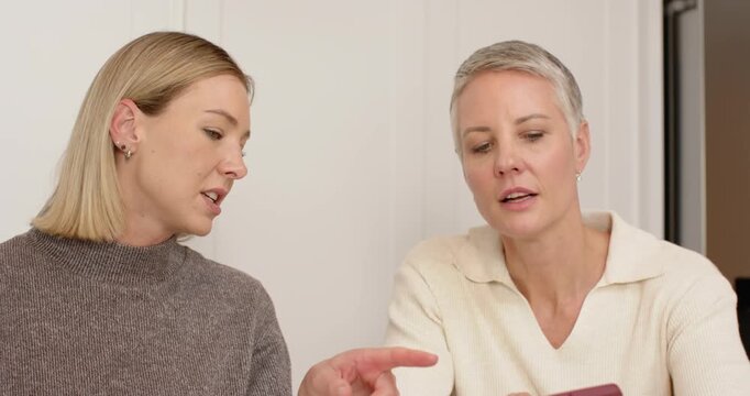 Mother and daughter picking up red smartphone tapping screen guiding walkthrough at kitchen table