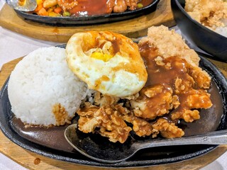 Sizzling plate of crispy fried chicken steak, white rice, and sunny-side up egg with gravy sauce
