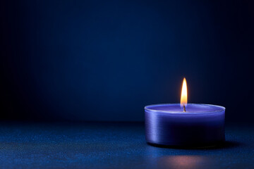 Small, dark blue tealight candle with a bright, flickering flame provides warm glow in deep darkness.