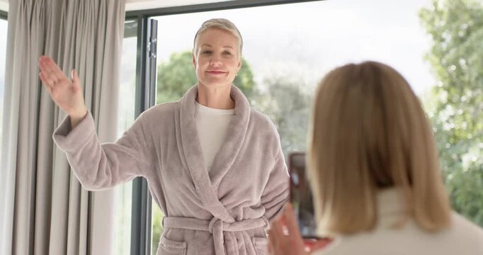 Adult daughter filming mother by glass door, waving kissing miming piano pointing phone playful