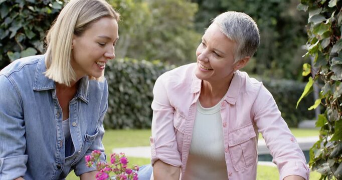 Starting with mother holding pot guiding daughter troweling soil at flowerbed planting pink blooms