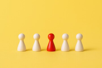 Obraz premium Red Game Piece Standing Out Among White Pawns on a Yellow Background Depicting Individuality