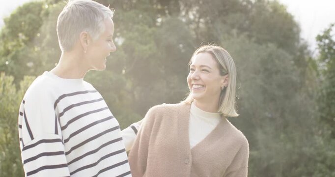 Mother and daughter smiling and laughing after mom slipping arm around shoulder in sunlit garden
