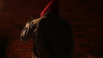 Criminal man in hood with gun near brick building outdoors, back view