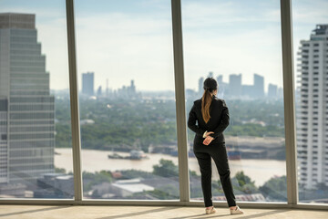 architect woman in suit thinking planning thoughtful inspection on empty office interior near glass window. office interior standing thinking planning thoughtful with blueprint on skyscraper floor