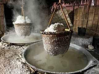 Traditional salt boiling process with baskets of crystallized salt hanging over steaming brine, showcasing rustic craftsmanship and local production methods