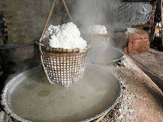 Traditional salt boiling process with baskets of crystallized salt hanging over steaming brine, showcasing rustic craftsmanship and local production methods
