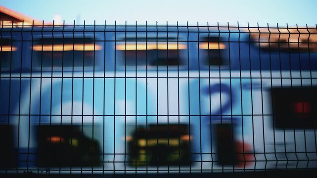 Blurred train passing behind a metal fence, creating an abstract transportation scene with strong graphic lines