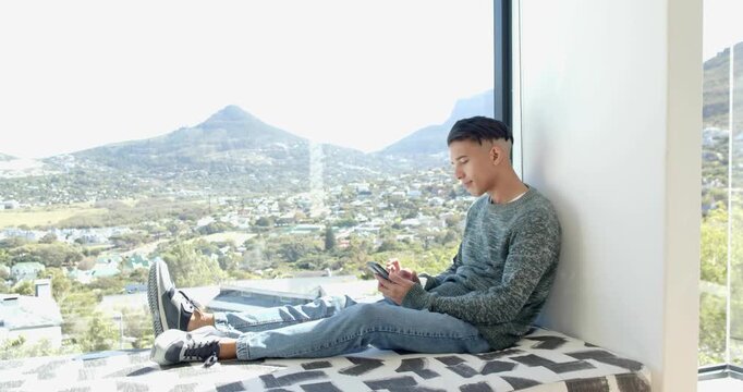 Man tapping smartphone on window bench and browsing, animating tech dashboard over valley view