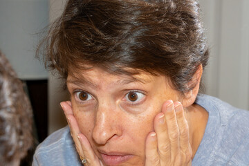 A woman in her early fifties looks in the mirror, concerned with her appearance. Beauty and aging concept