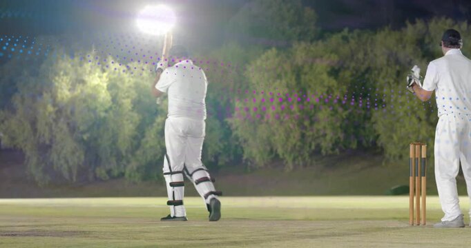 Cricket bowler releasing ball batsman playing clipping pads fielders confirming wicket under lights