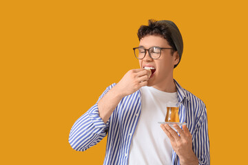 Young man with Turkish tea eating delight on yellow background