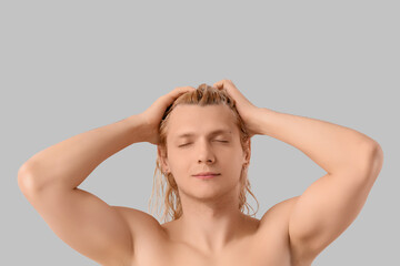 Fototapeta premium Young blonde man washing hair on light background