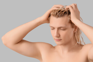 Fototapeta premium Young blonde man washing hair on light background, closeup