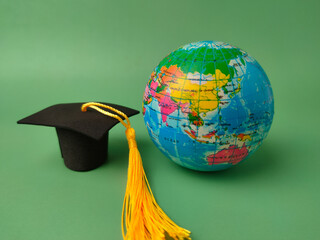 Miniature graduation cap and a small globe against a green background