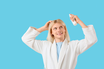 Fototapeta premium Young blonde man with hair spray on blue background